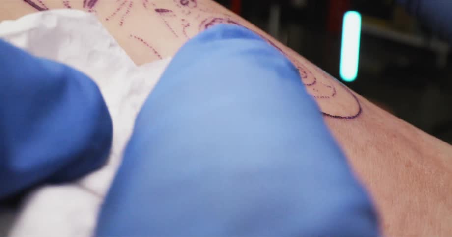 Tattooist wears gloves while wiping fresh tattoo leaving an ink smear