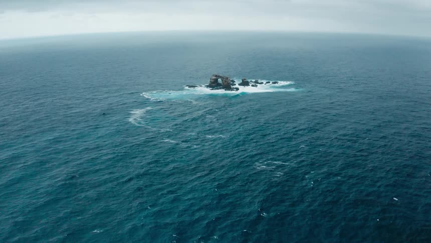 An islet in the ocean surrounded by water with the sky and clouds in the background