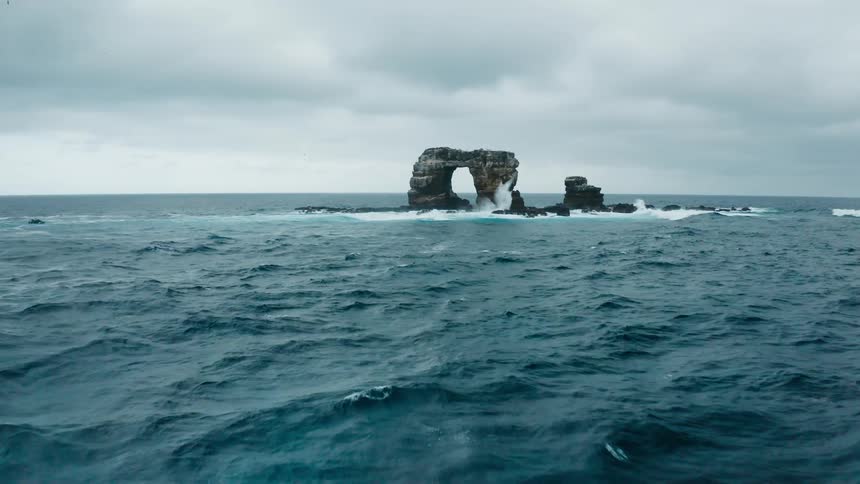 Waves splashing against a natural arch rock formation under a cloudy sky