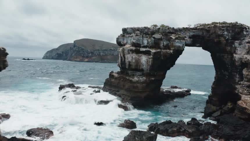 Aerial view of a natural rock arch in the ocean in front of an island