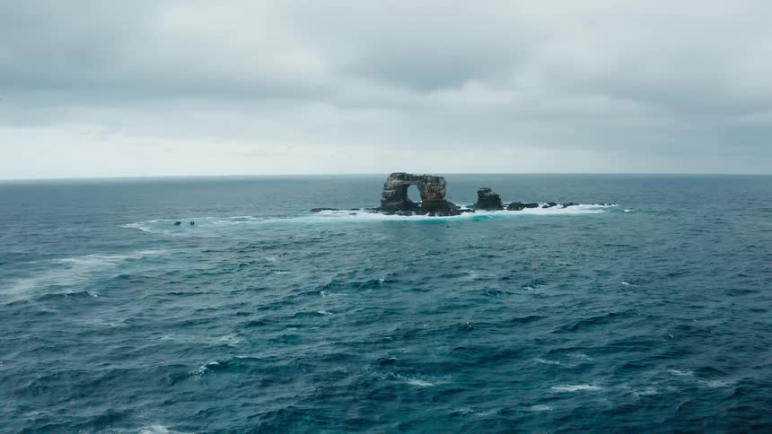 Waves splashing against a natural arch rock formation under a cloudy sky