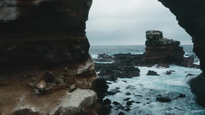 Ocean waves splash and churn against rock formations on a gray cloudy day