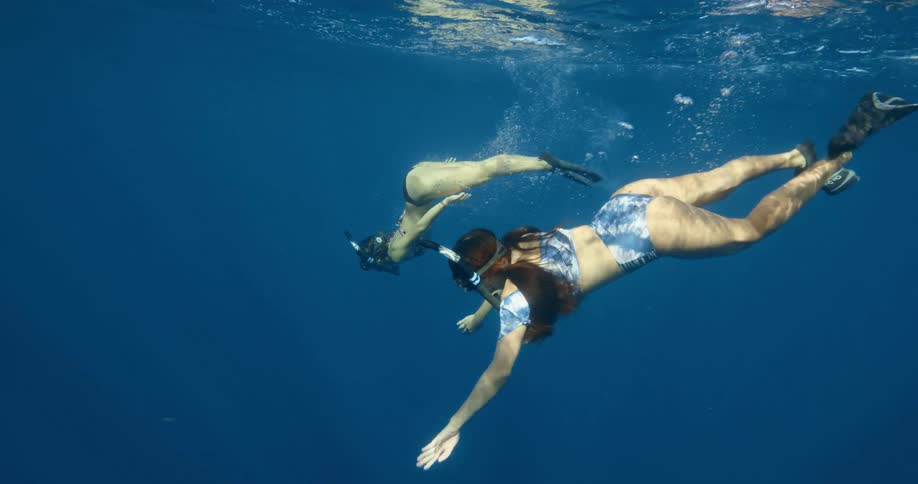 Two women with snorkels and flippers swimming underwater