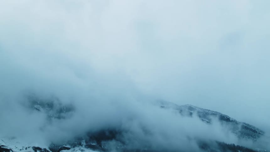 A rocky mountain is shrouded in clouds on a cold winter day