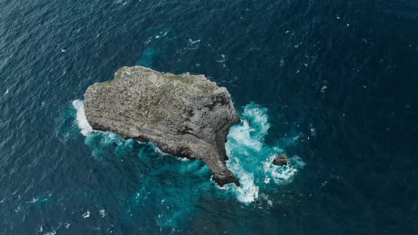 White of crashing waves contrasts with blue of ocean gray stone of island