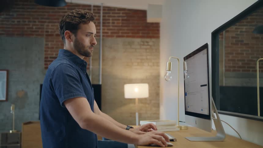 Man with a beard and a blue shirt works on imac desktop