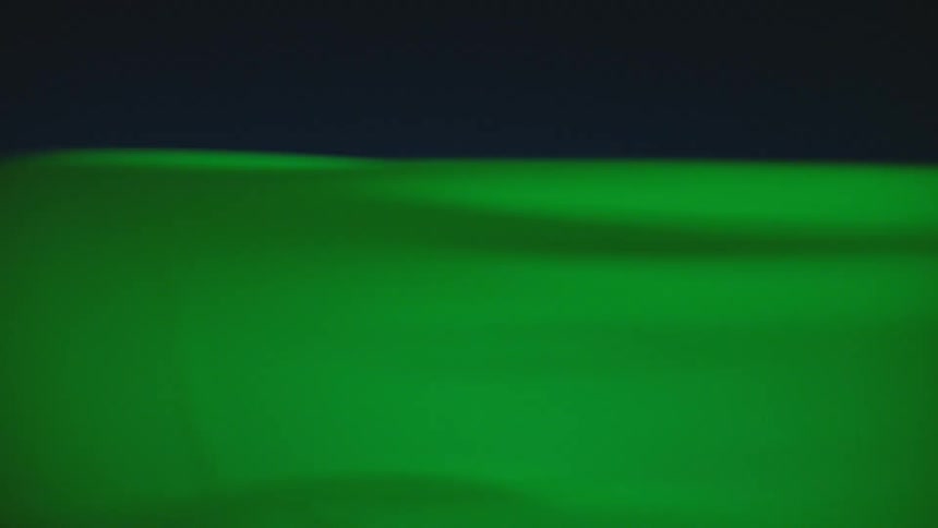 A green sheet waving in the wind with the sky and clouds in the background
