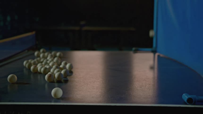 Ping pong balls bouncing on a ping pong table in a room with a wall in the background