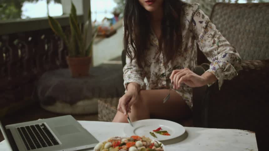 Woman uses a fork to eat food from a plate while sitting on an outdoor porch