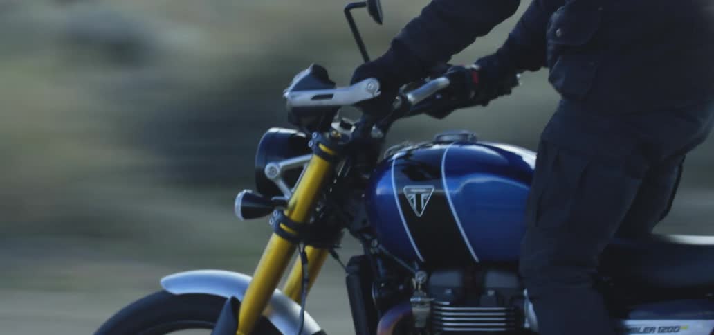 Rider stands on motorcycles while piloting cycle past scrub