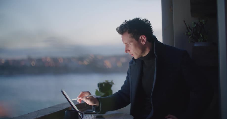 A man is sitting at a table and looking at a laptop