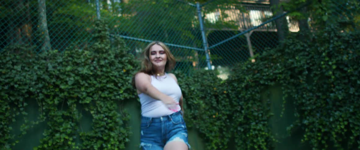 A teenage girl dances in a park in a neighborhood