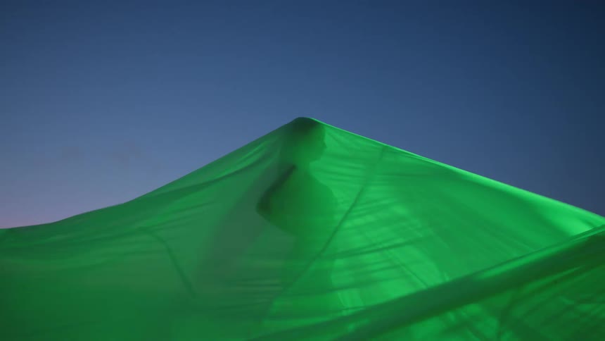 A person stands under the flowing green tarp