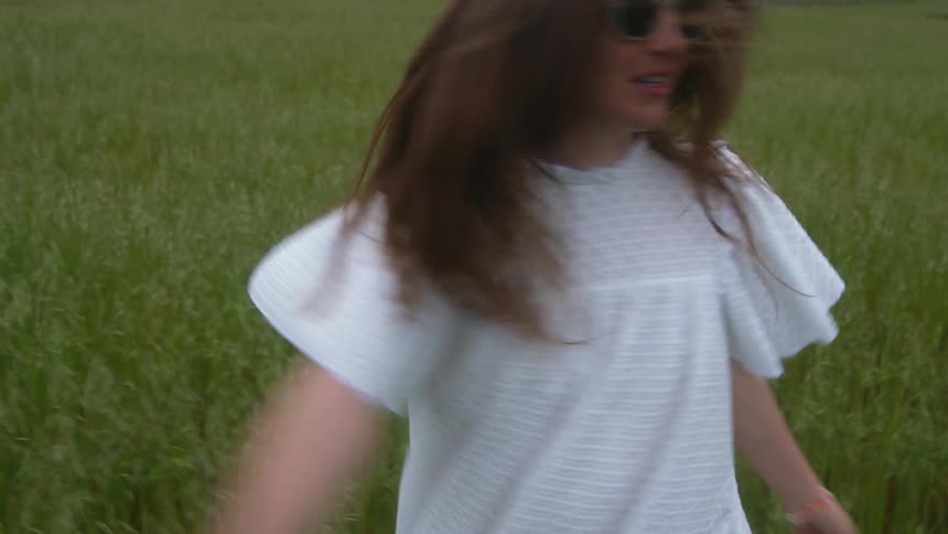 Woman twirling around in a field of tall grass during the day