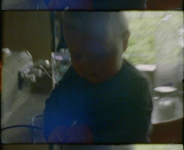 A vintage film of a baby sitting on a counter with his mom grabbing strawberries