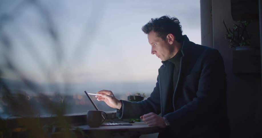A man stands at a small table and uses a pen to touch things on a tablet computer