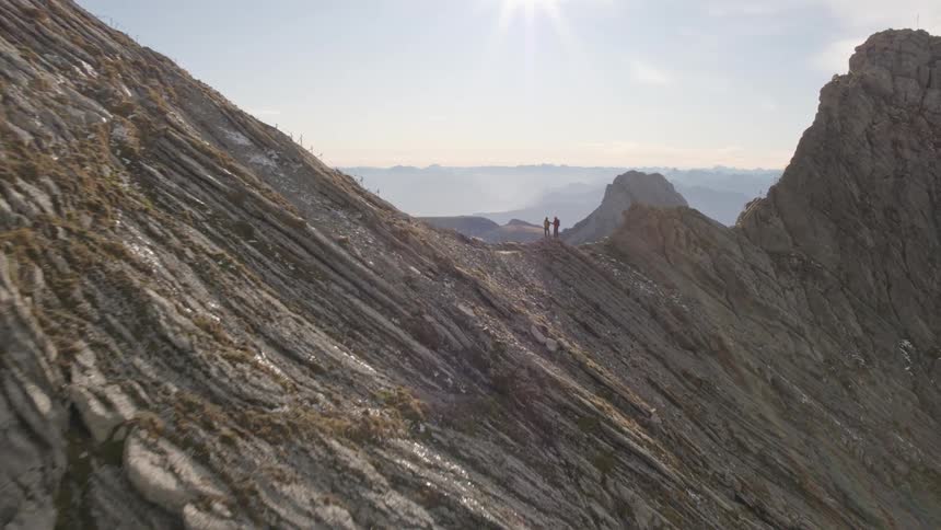 Two people standing on top of a mountain ridge with mountains in the distance