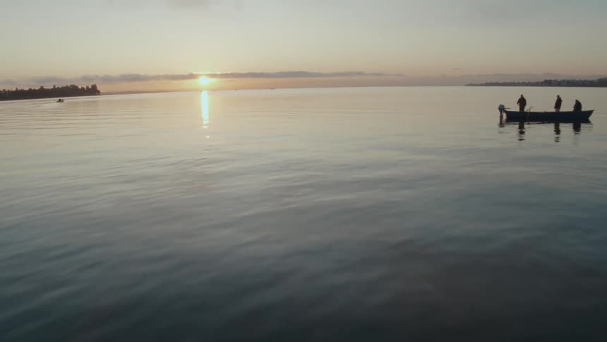 Three people on a boat on a calm lake at sunset