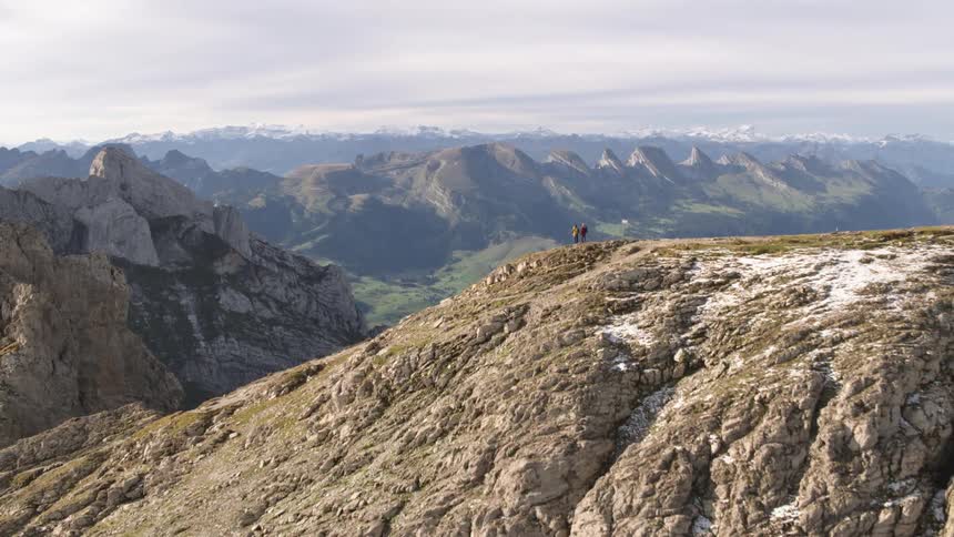 Two people stand on a cliff overlooking a vast canyon