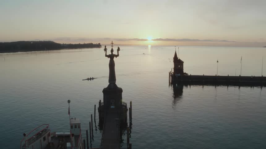 Aerial view of a statue at the end of a pier at sunset