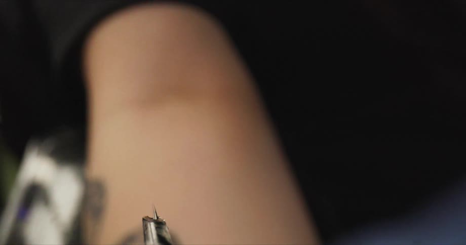 A tattoo artist moves the needle towards the person's arm