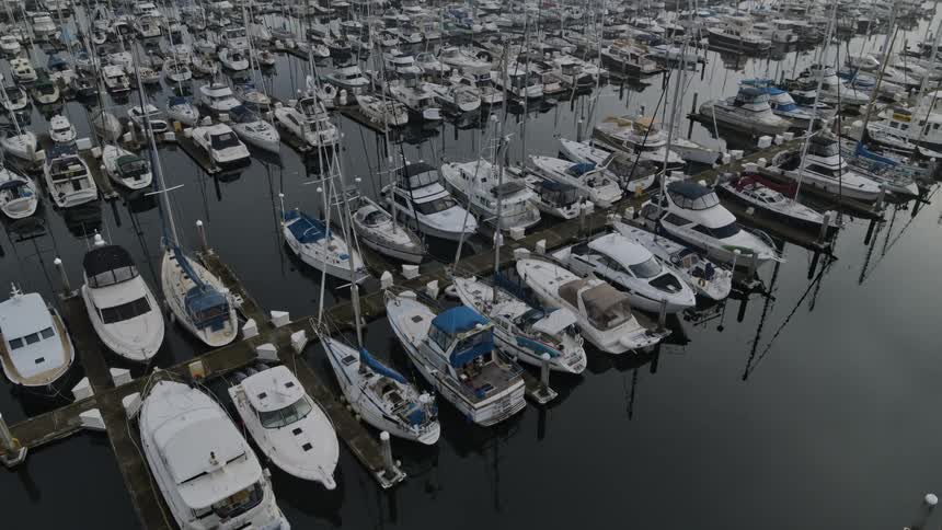 Slow pullback reveal of sailboats and motorboats docked at a marina on a foggy day