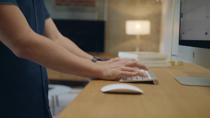 A man stands in front of a computer monitor and types on a keyboard