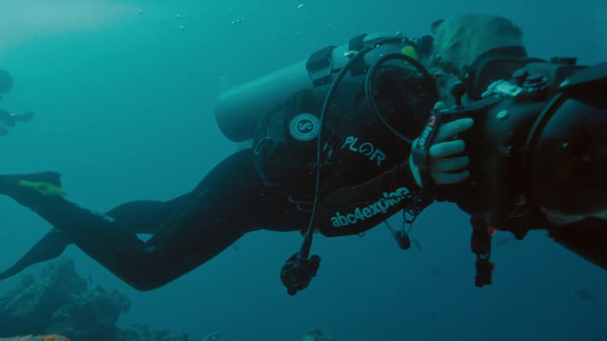 Scuba divers swim near reef as one pushes underwater camera along
