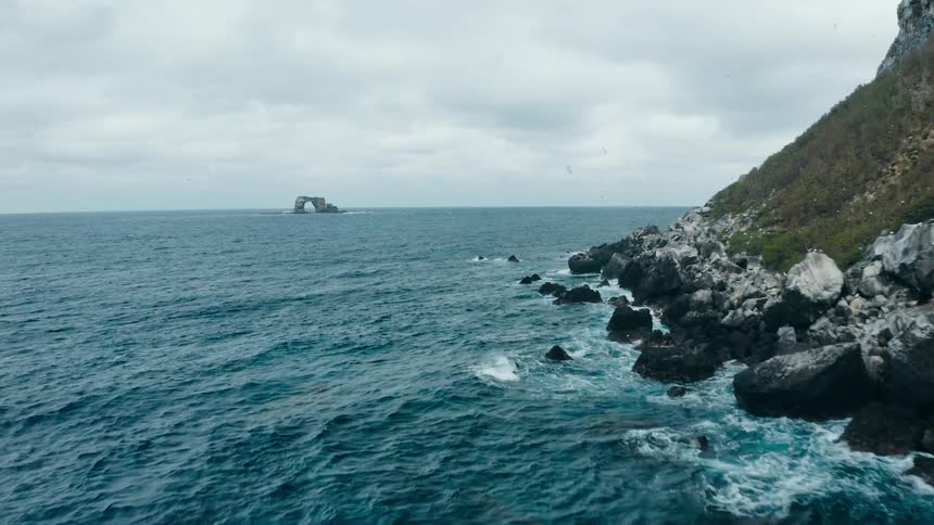 A rocky coast with birds flying with an islet the sky and clouds in the background