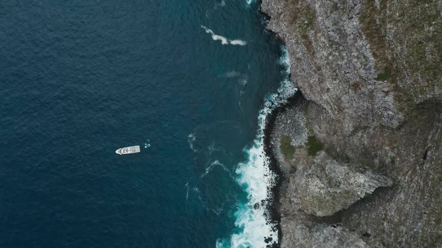 A large cliff on the shore with a boat in the water