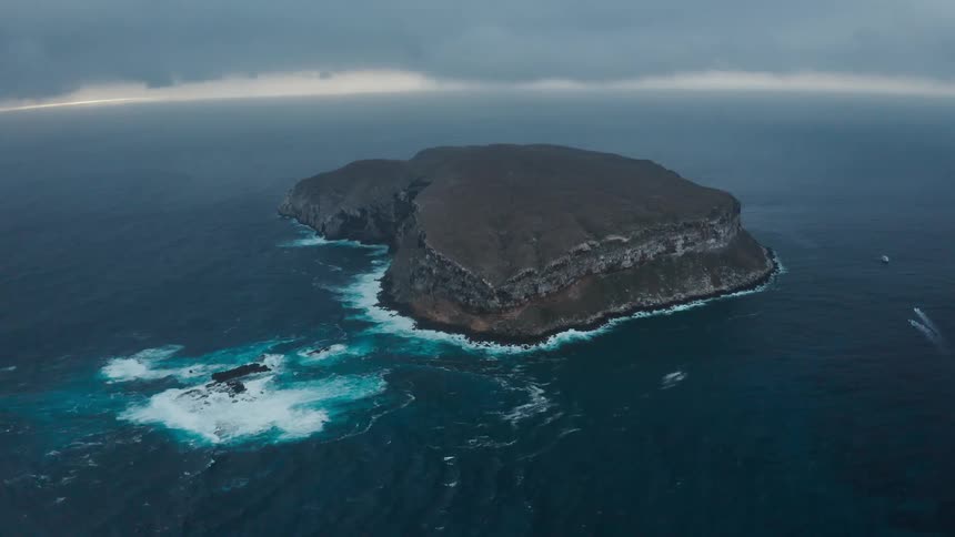 An island in the ocean with rippling water with the sky and clouds in the background