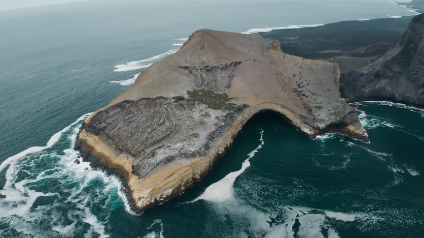 A peninsula in the ocean with waves of water with the sky and clouds in the background