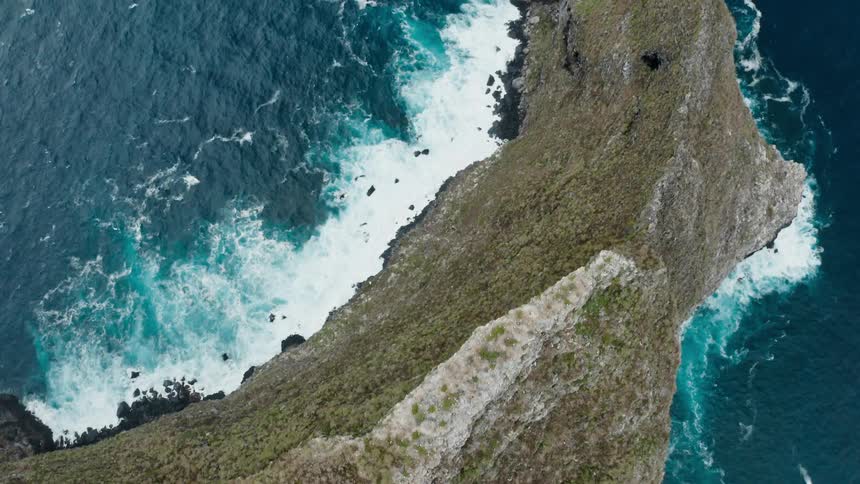 Ocean waves splash against the rock formations as gulls fly