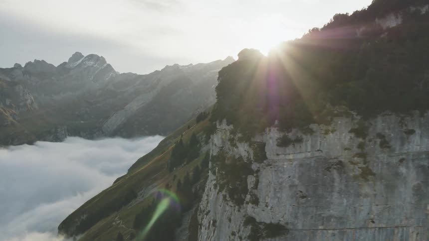 Snow covered mountain peaks high in the sky with the sun shining brightly through the clouds