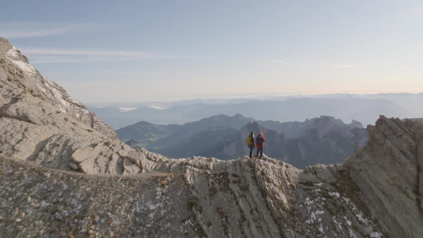Two people standing on the barren mountaintop looking at the valley at morning