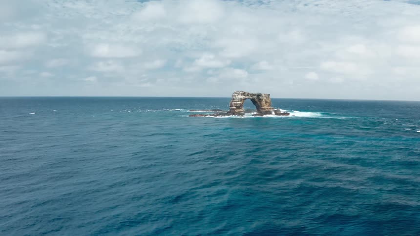 Natural arch rock formation in the ocean under a cloudy sky