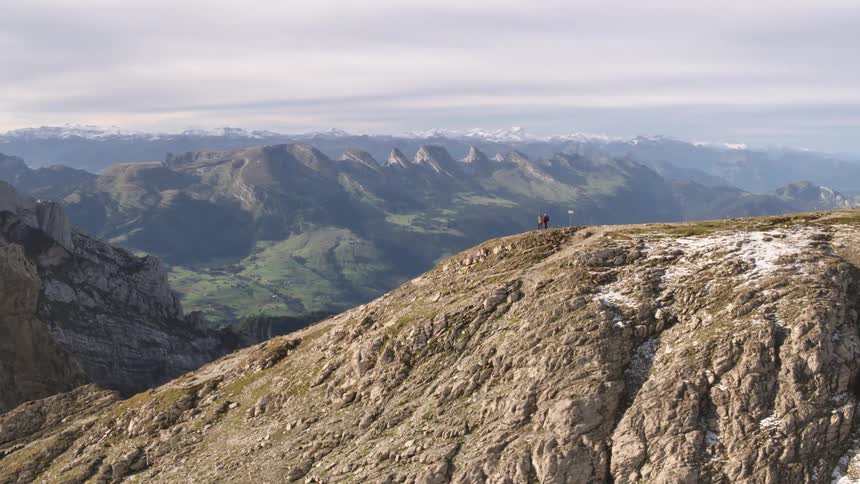Two people stand at the edge of a plateau and look over a vast canyon