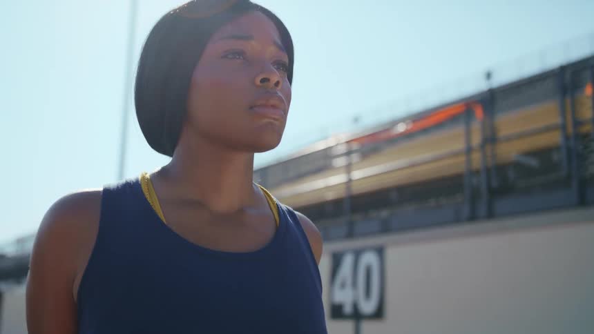 A woman stretches and takes deep breaths in a stadium waiting to begin to run