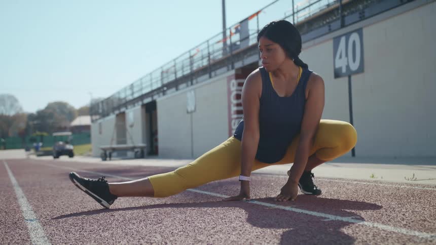 Black female athlete stretches her leg while crouched on the track