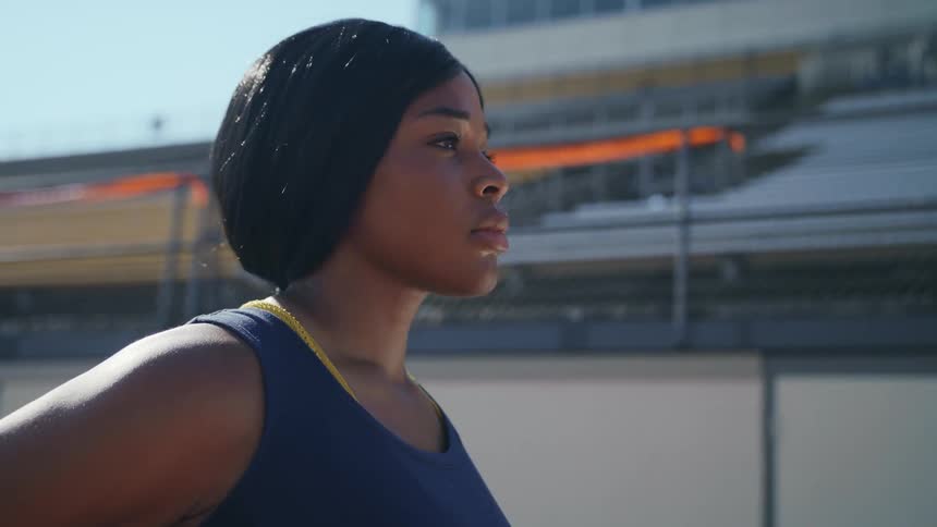A woman stands on a track with no people in the bleachers behind her