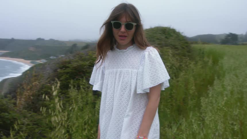 Woman walks away from top of hill overlooking beach and ocean