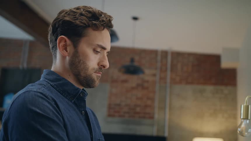 Man with a beard and blue shirt stands and uses imac desktop