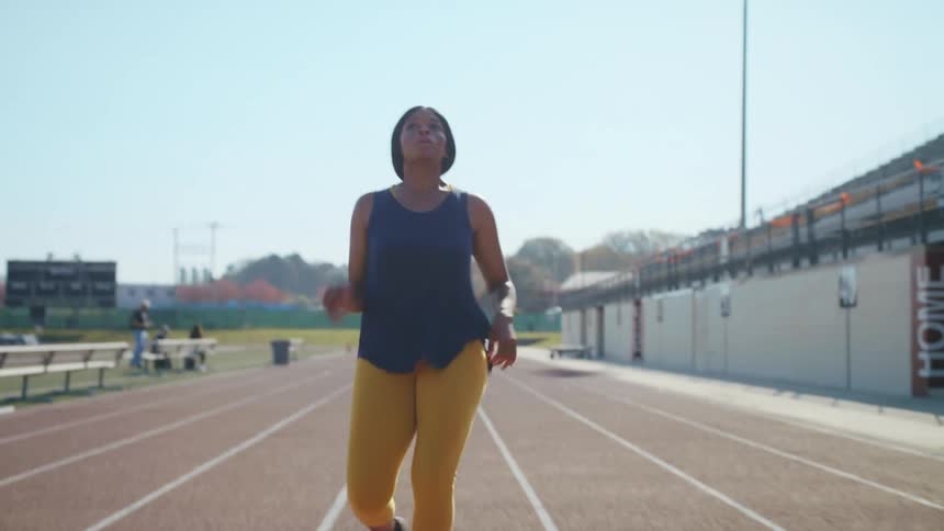A woman running on a running track with the sky and clouds in the background