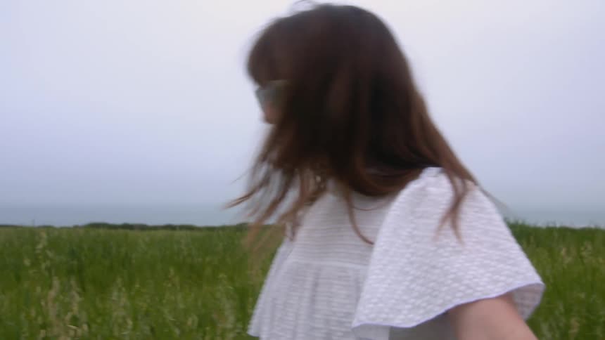 Young woman wearing sunglasses and a white dress playing on a grass field