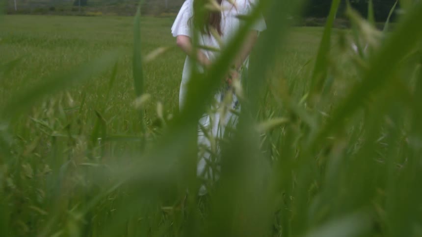 Woman with brown hair and white dress walks in grassy field