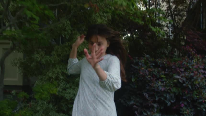 A woman runs outside her house in her nightgown and laughs and swings her arms forwards
