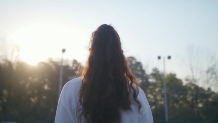 A woman walks into a tennis court with a duffle bag in her hand
