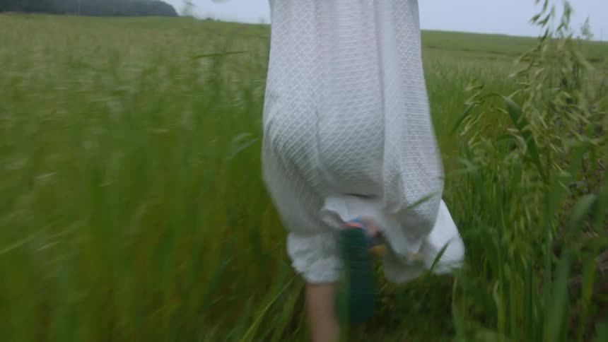 Young woman wearing sunglasses and a white dress running on a grass field