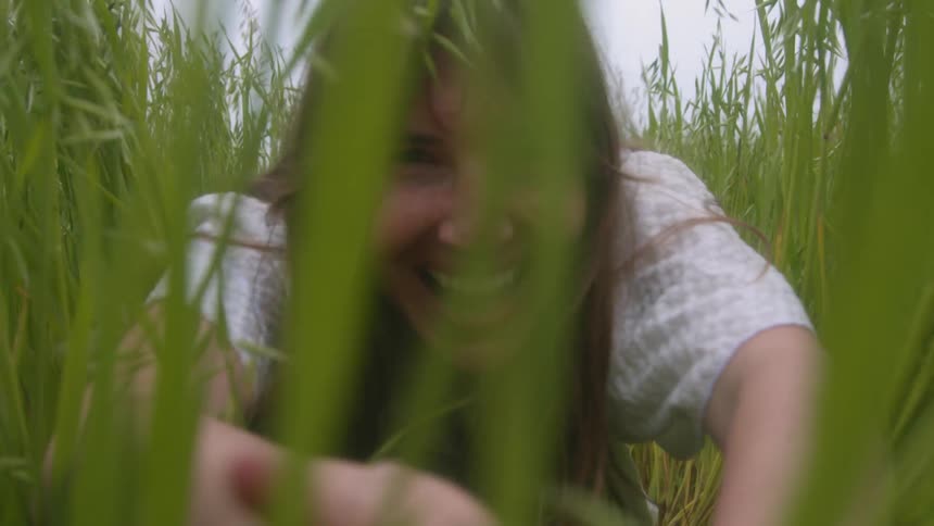 A woman pushes back tall grass in a rural field with a large smile on her face