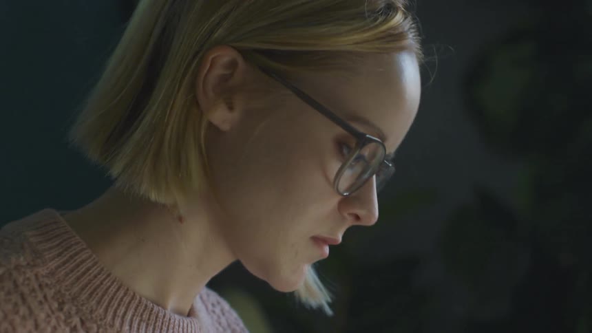 Blonde woman wearing glasses combs hair back as she focuses on work